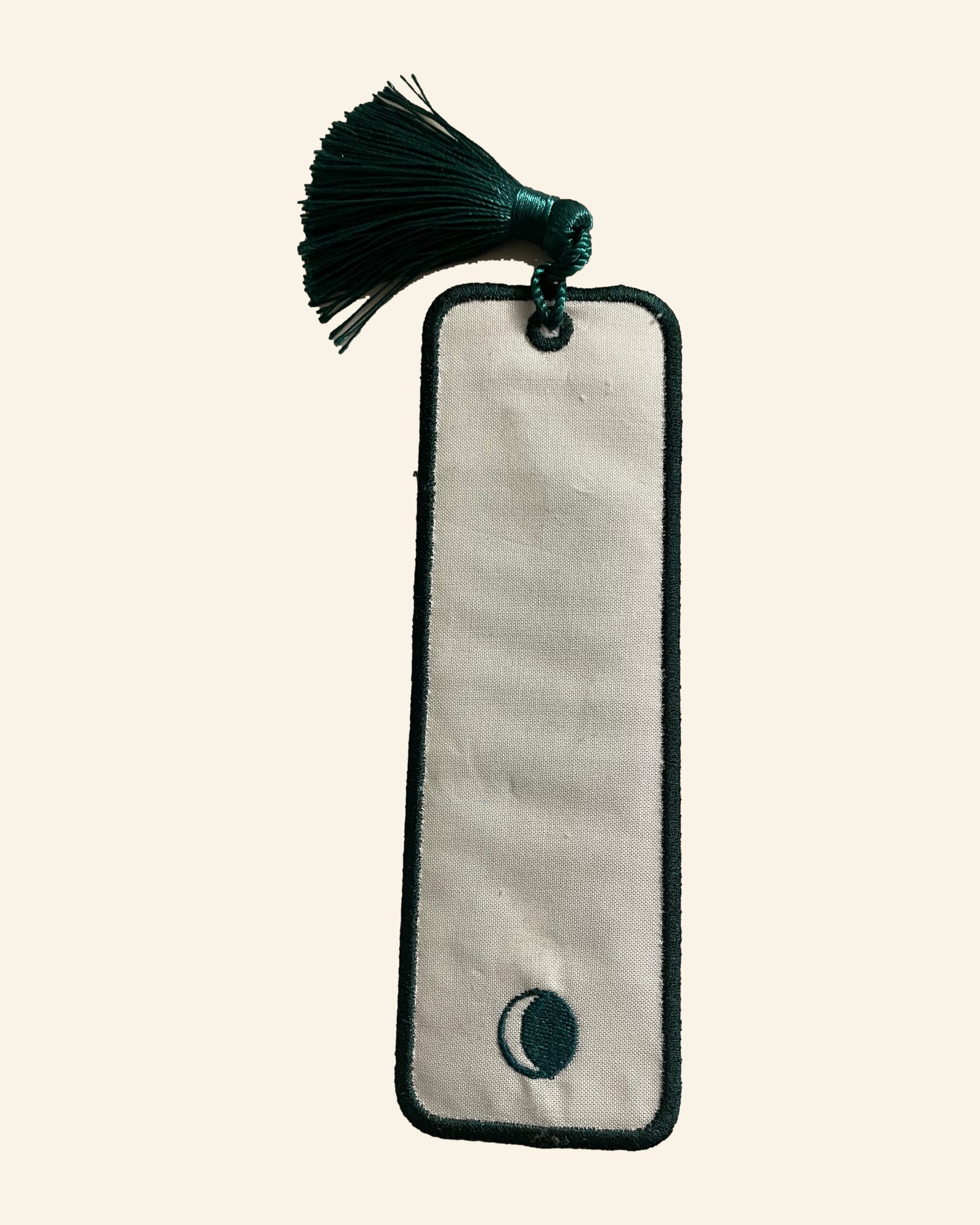 The back of the bookmark: plain cream with the green border and a small embroidered moon near the bottom.