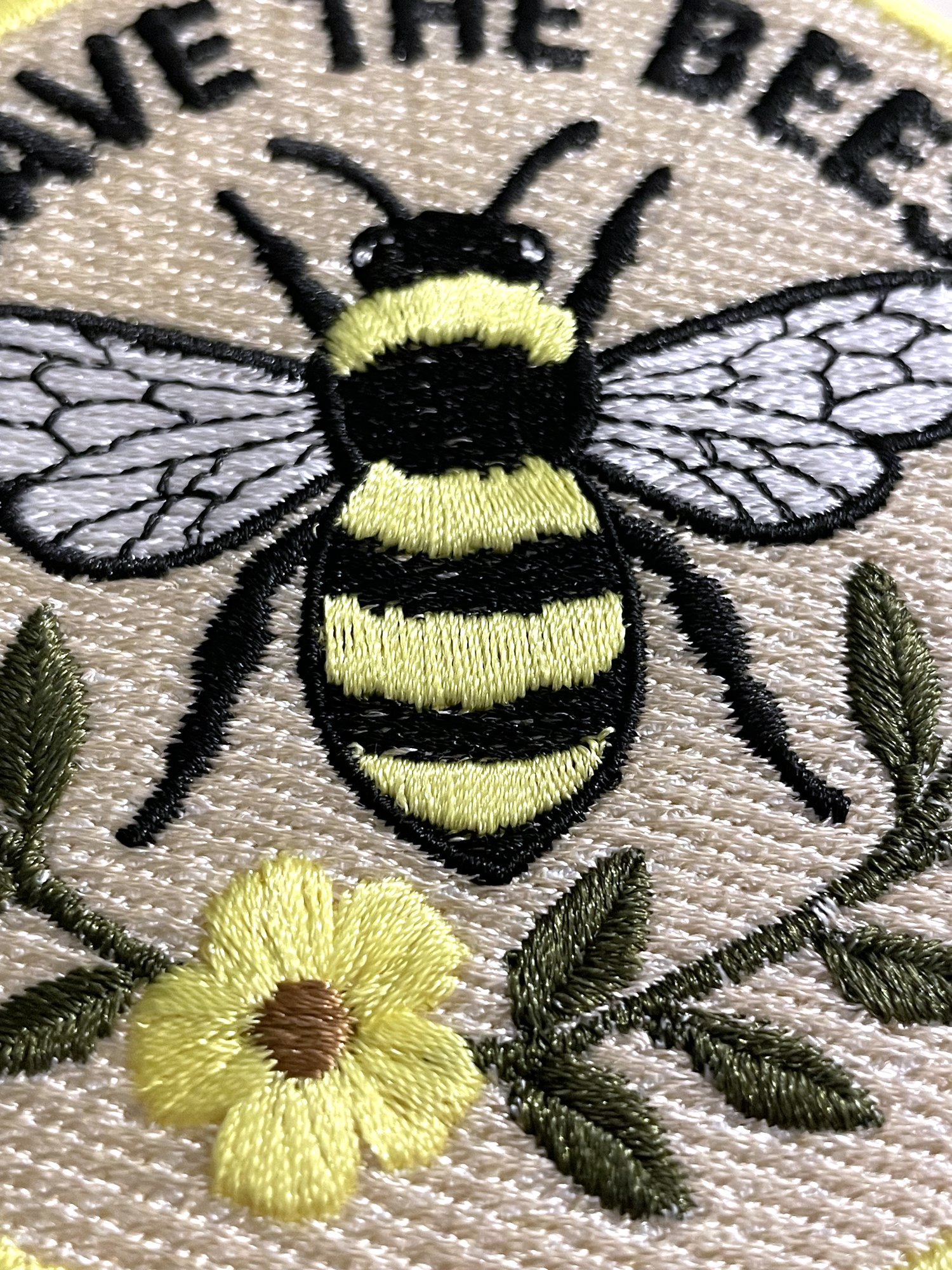 A close-up of the patch at an angle, showing the texture of the stitched bee, wings, flower and leaves.